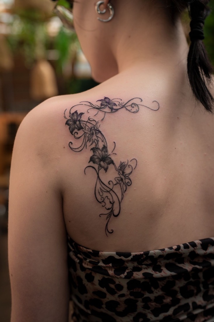 Fine line florals and fairies across a shoulder and collarbone, by Tuba at THRONE Northampton