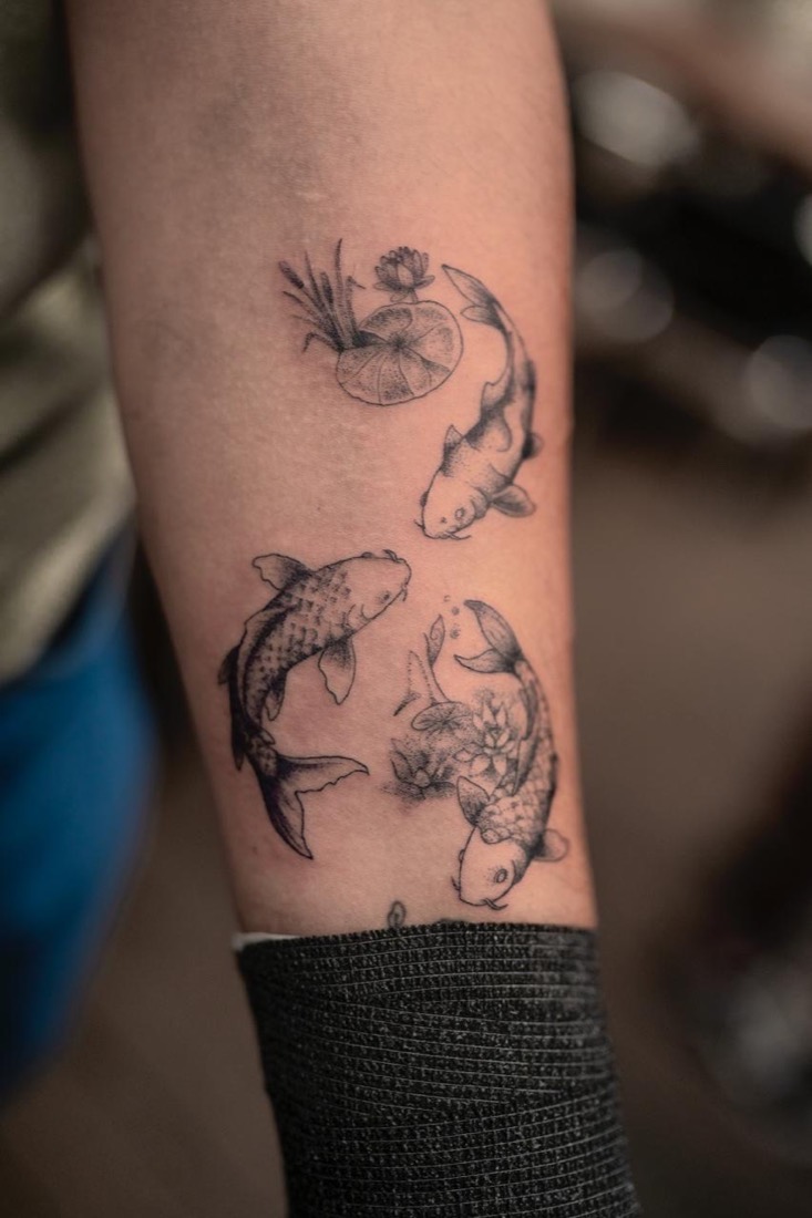 Three koi and a lily pad in fine dotwork on a forearm, by Tuba at THRONE Northampton